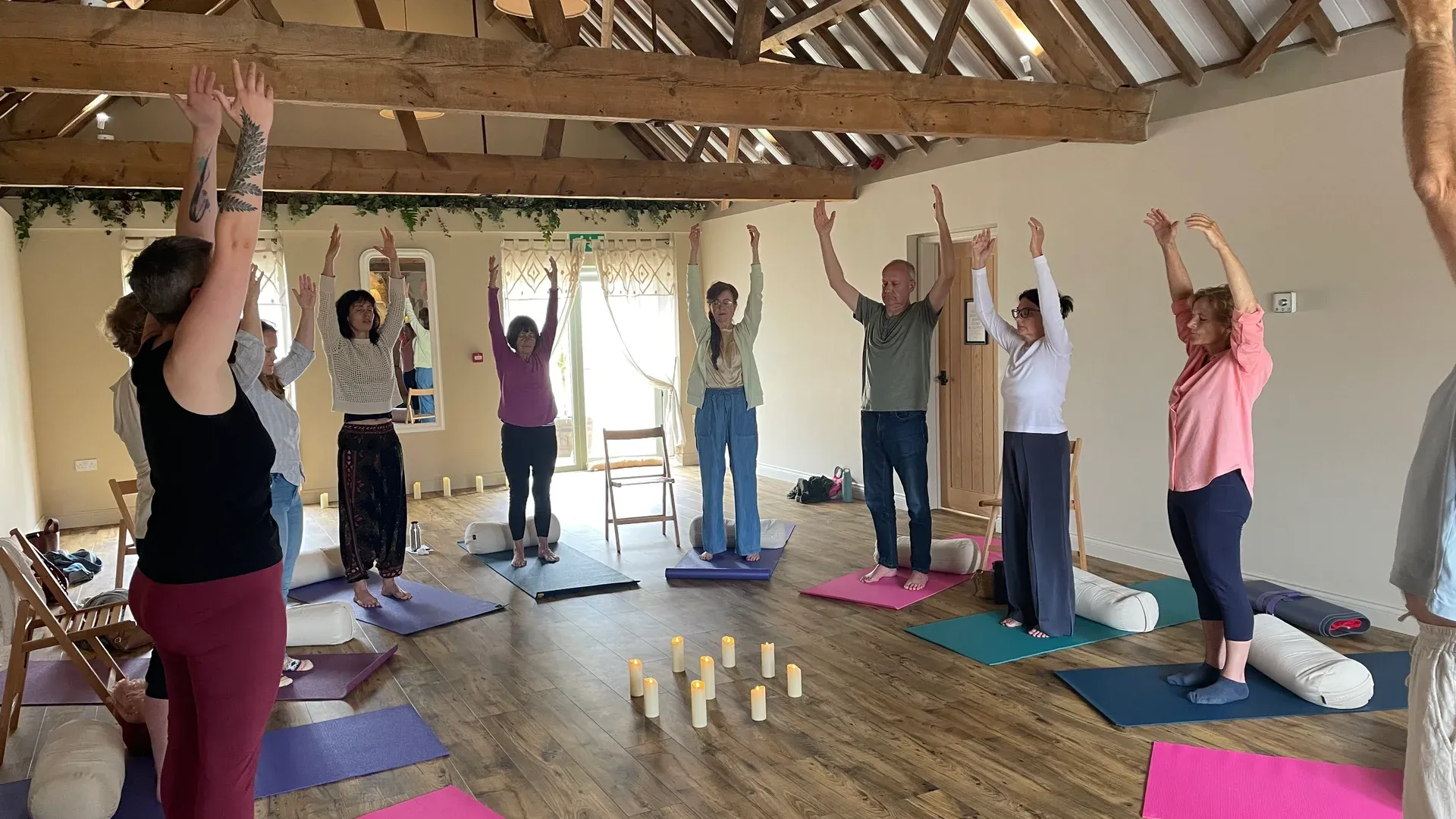 The workshop group standing in talasana, arms raised overhead, in a circle around candles at The Painted Barn